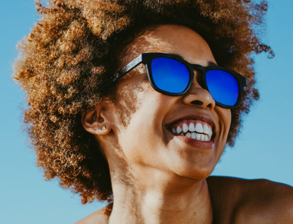 Person with curly hair wearing Glasses with Transitions&reg; Lenses under blue sky