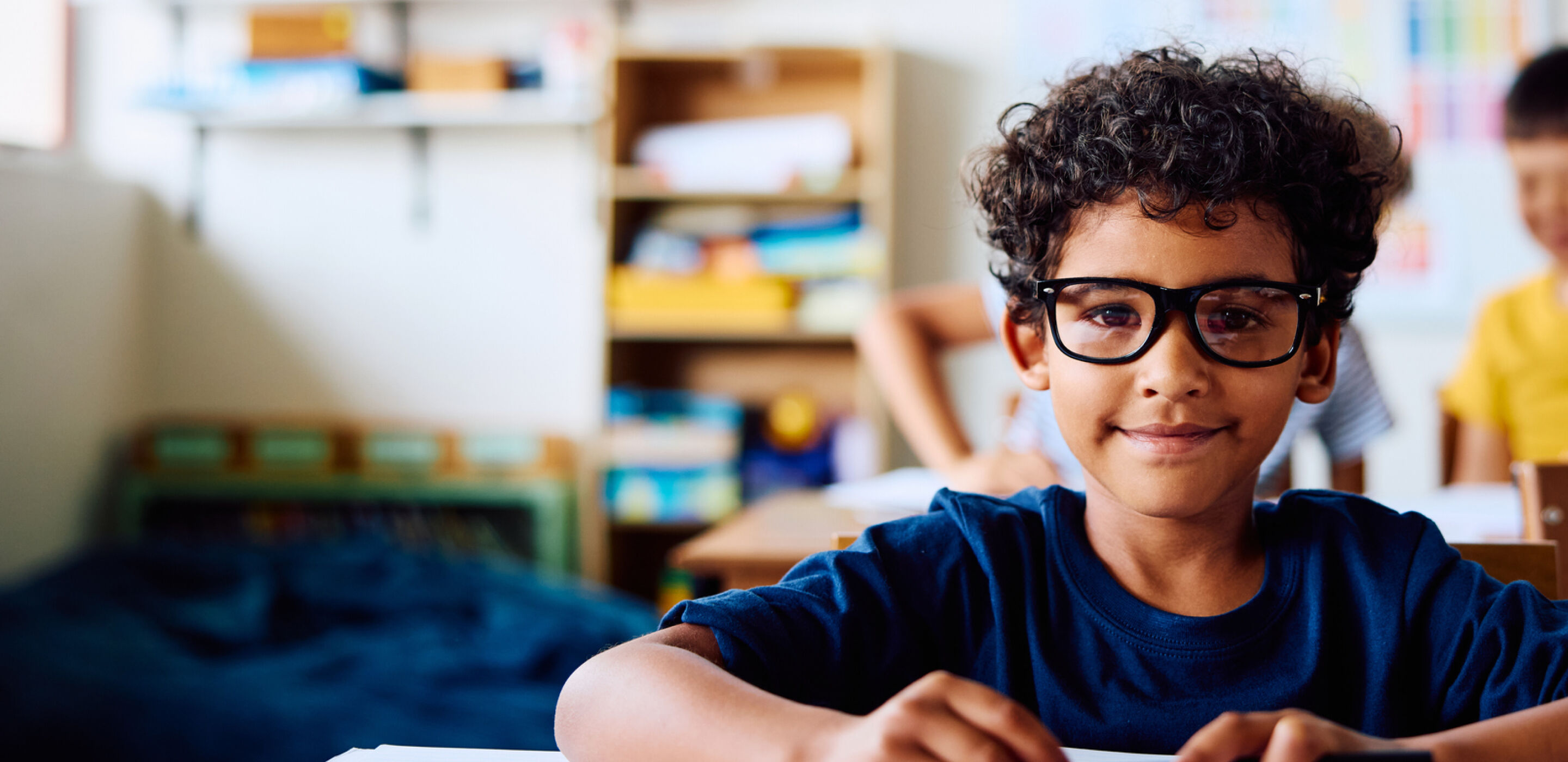 Child with dark hair in pigtails wearing round glasses, looking thoughtfully to the side.