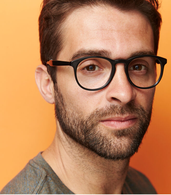 Man with glasses and beard against an orange background, reflecting healthy eye care at Boots Opticians