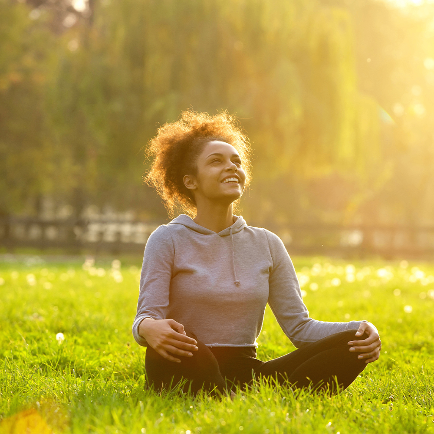 Woman sitting on grass in warm sunlight, smiling and enjoying a calm outdoor moment