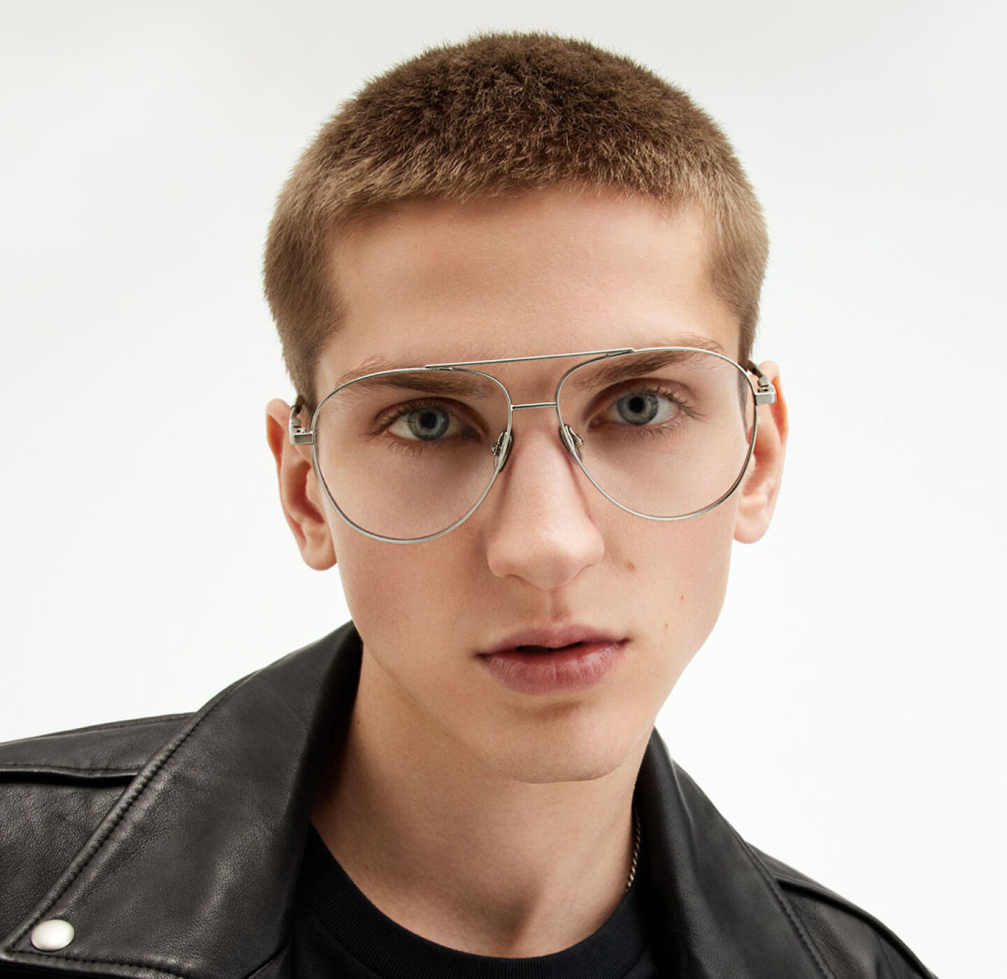 Young man in silver aviator AllSaints glasses and black leather jacket against a plain white background