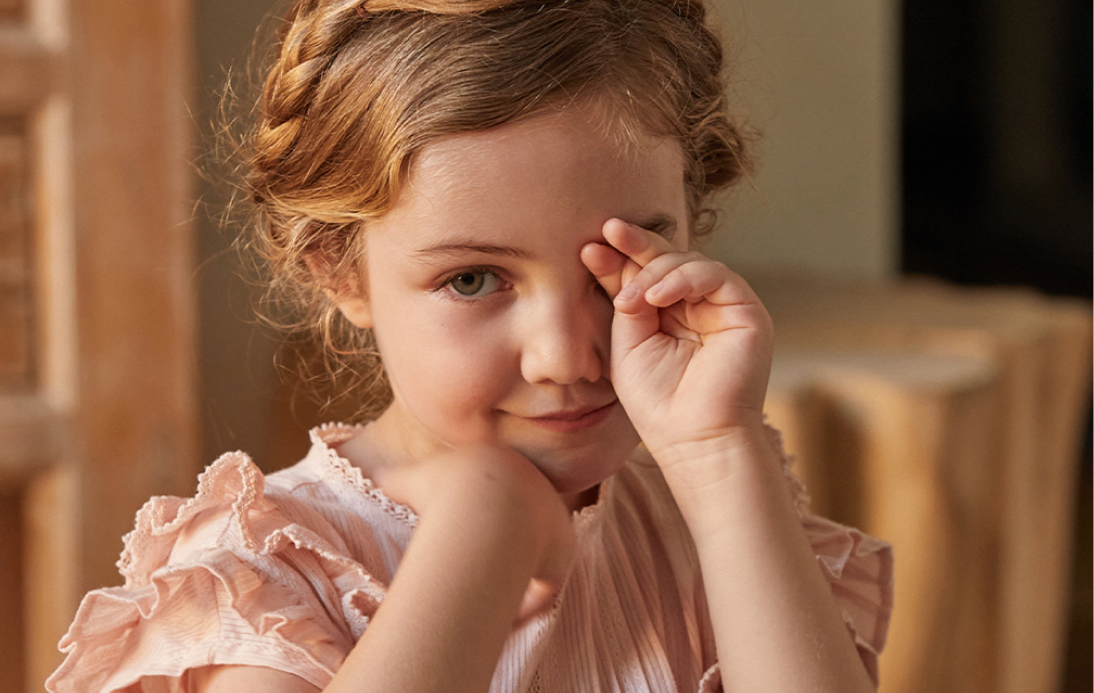 Young girl playfully covering one eye, smiling, illustrating a fun eye check experience.