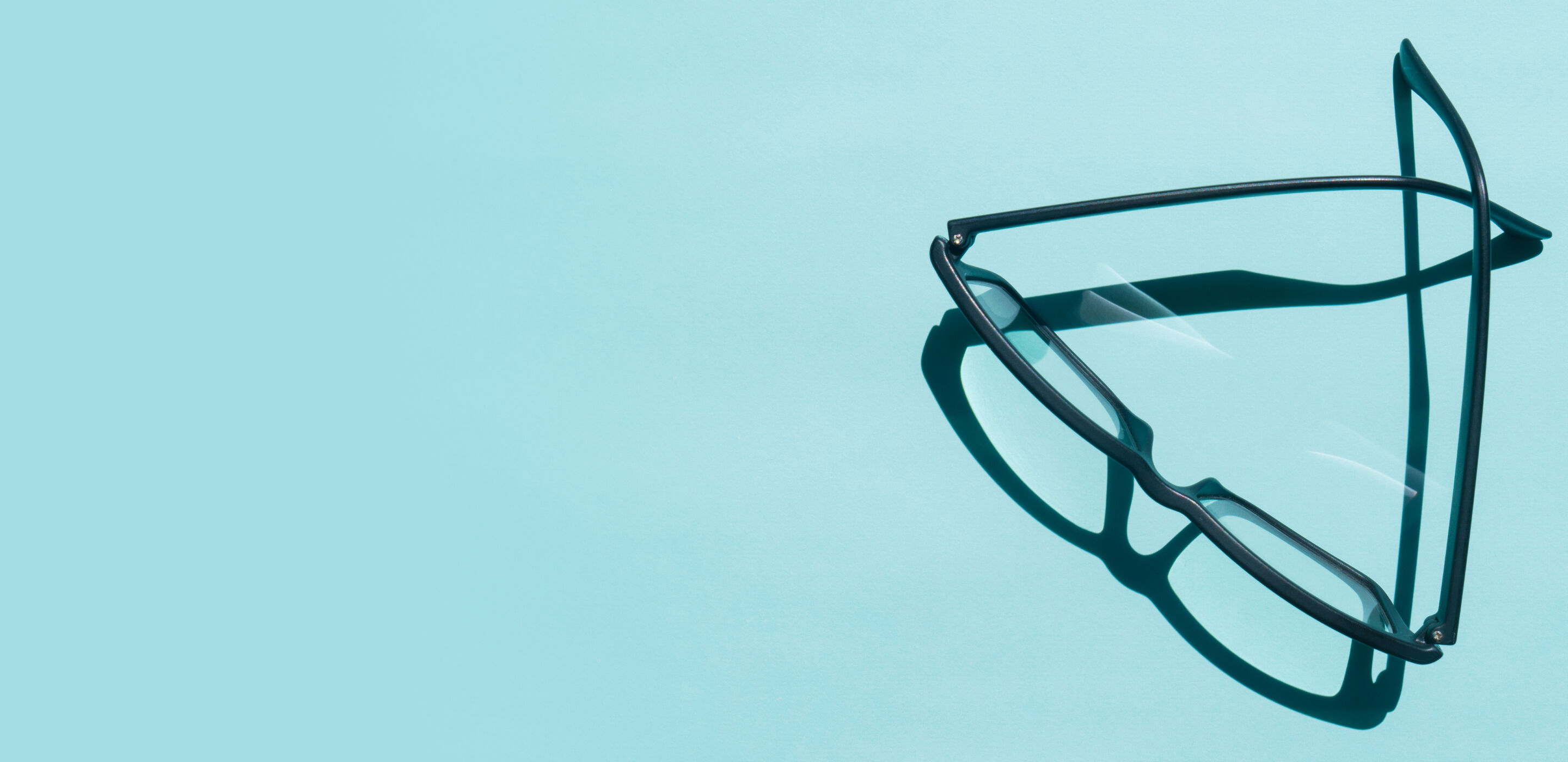 Black-framed eyeglasses casting a shadow on a light blue surface, representing blue light lenses at Boots Opticians