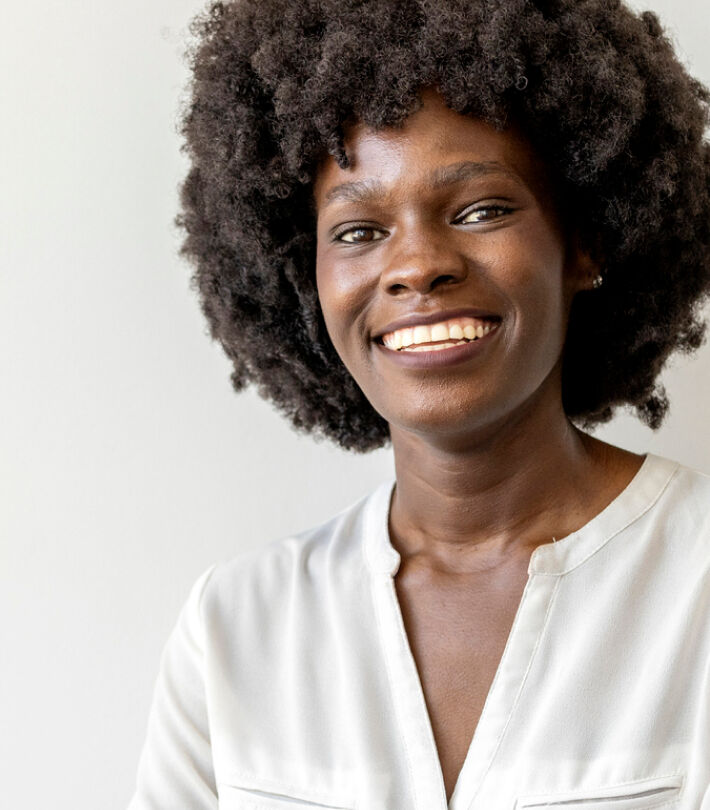 Smiling woman with curly hair in a white blouse, standing confidently wearing contact lenses