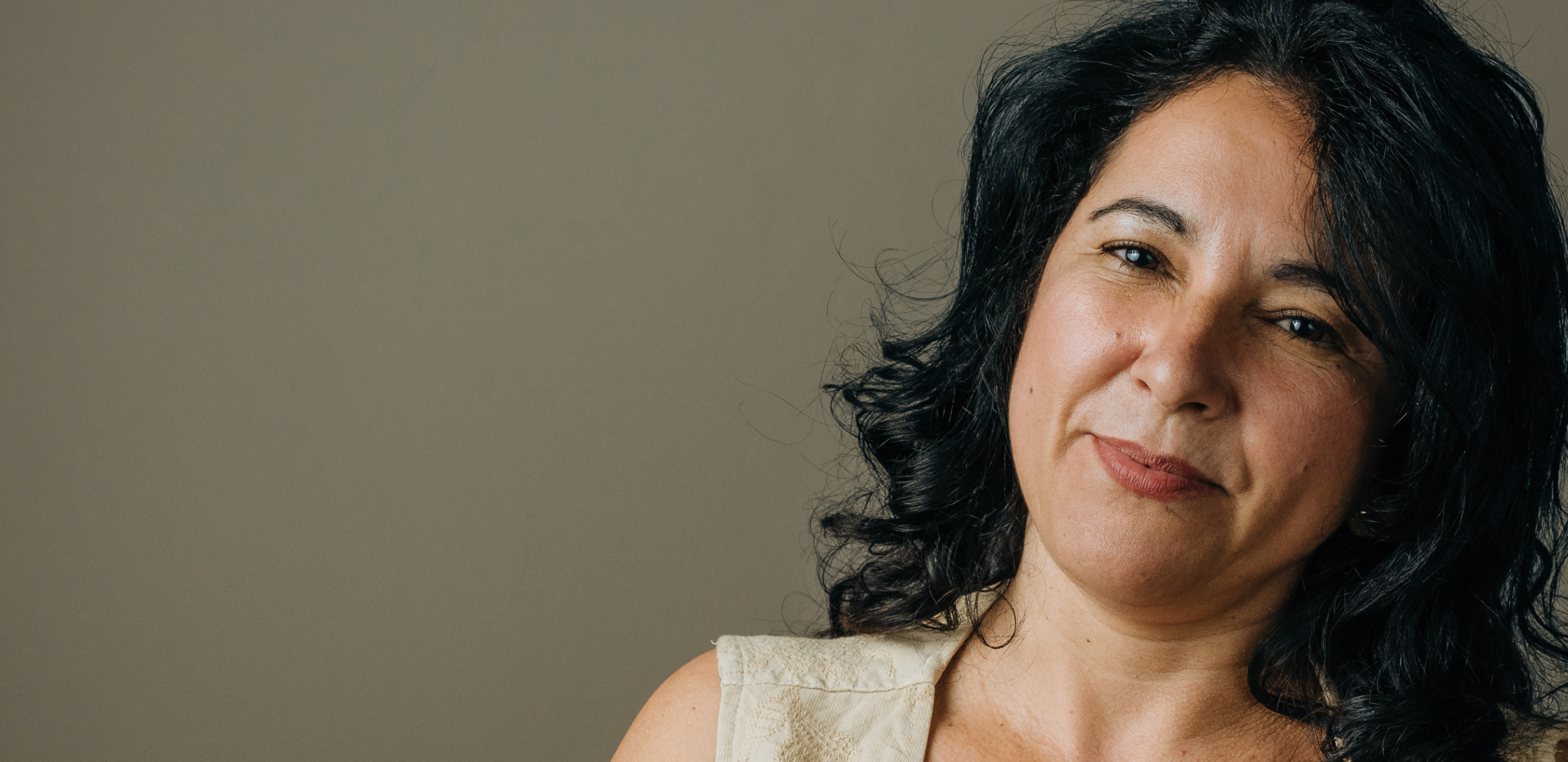 Woman with dark curly hair smiling warmly, representing comfort during a dry eye evaluation.