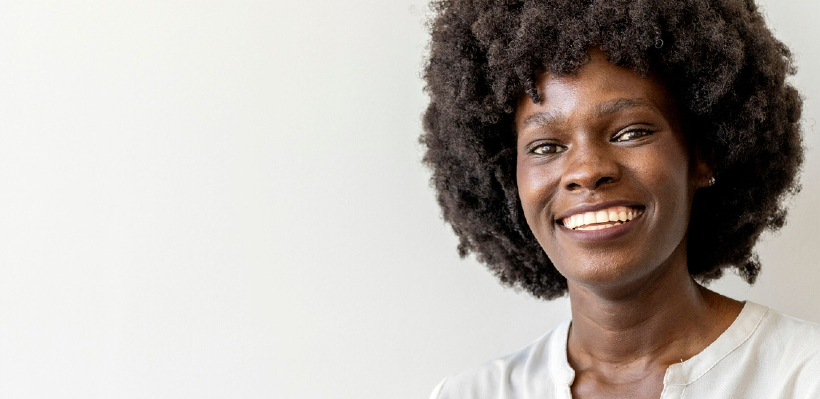 Smiling woman with curly hair in a white blouse, standing confidently wearing contact lenses