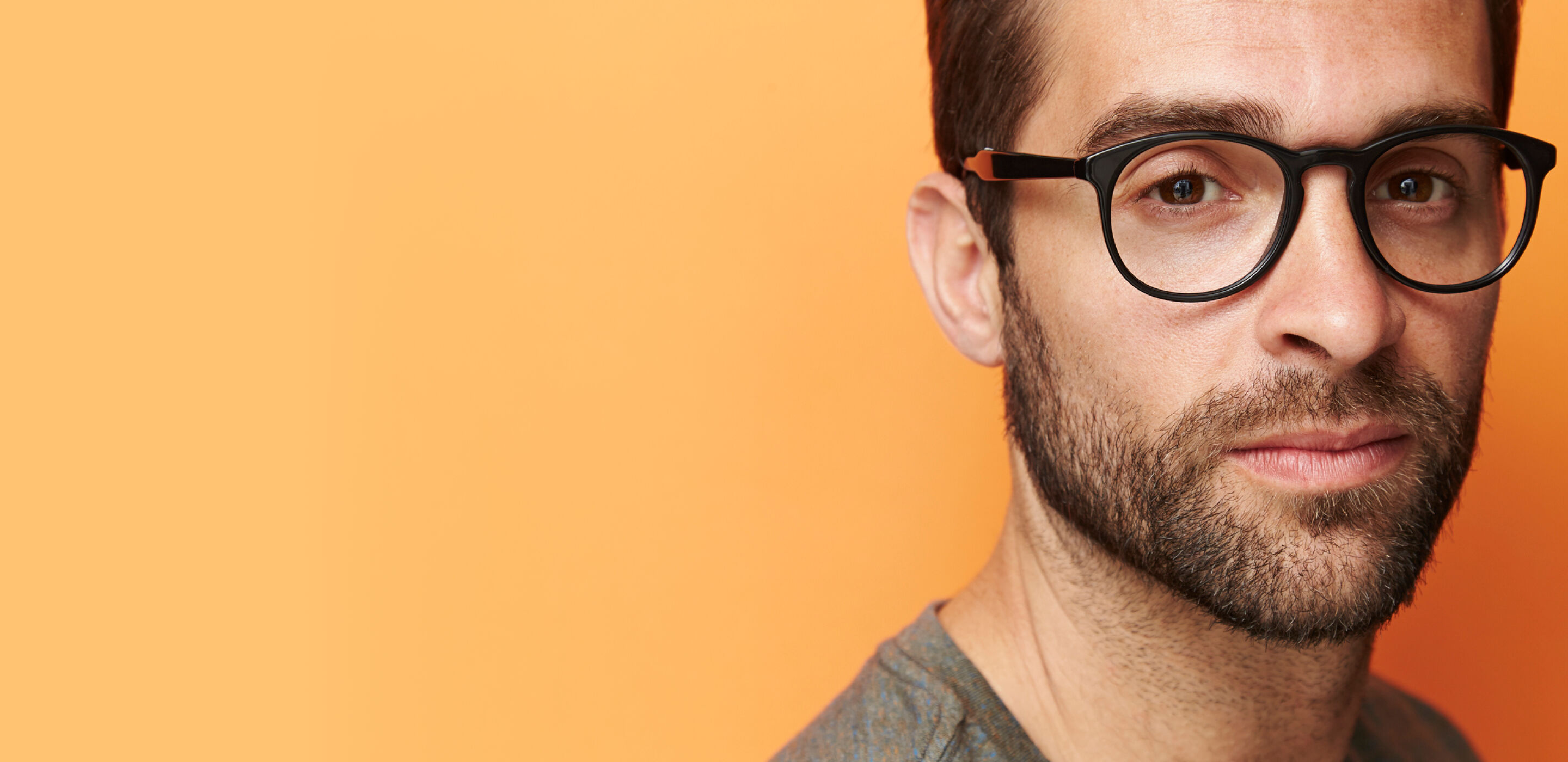 Man with glasses and beard against an orange background, reflecting healthy eye care at Boots Opticians