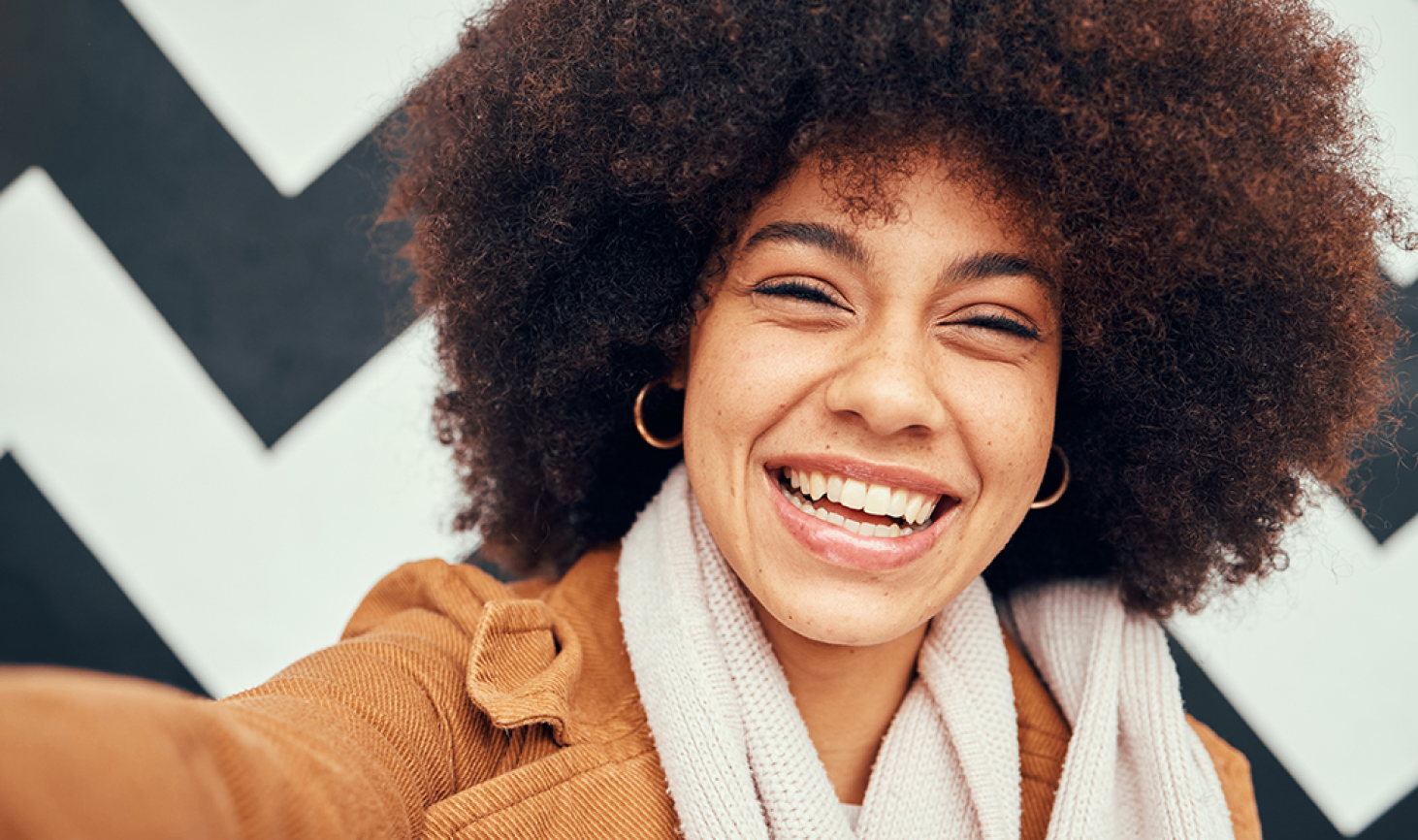Smiling women with curly hair taking a selfie against a black and white zigzag background.