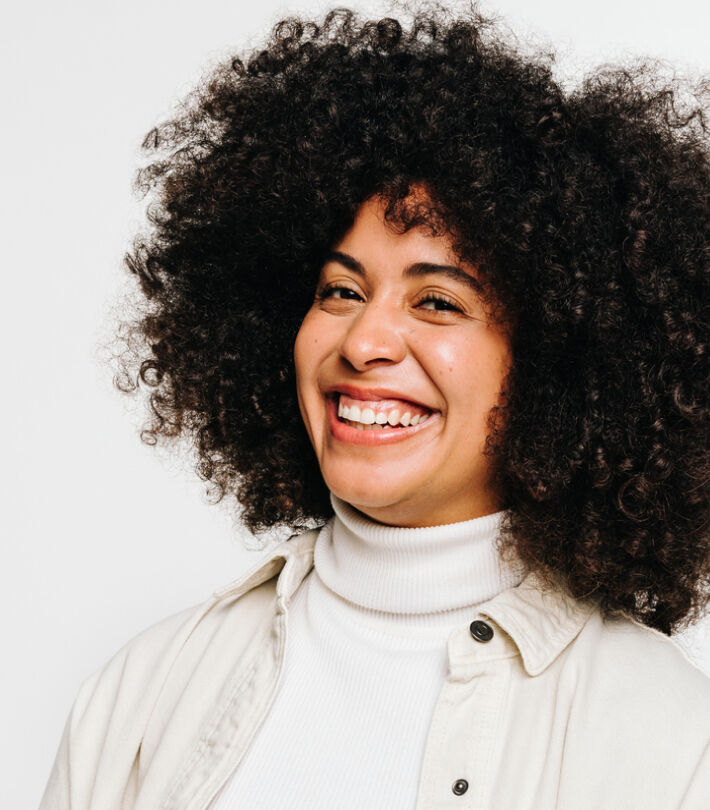 Smiling person with curly hair wearing contact lens against a clean white background