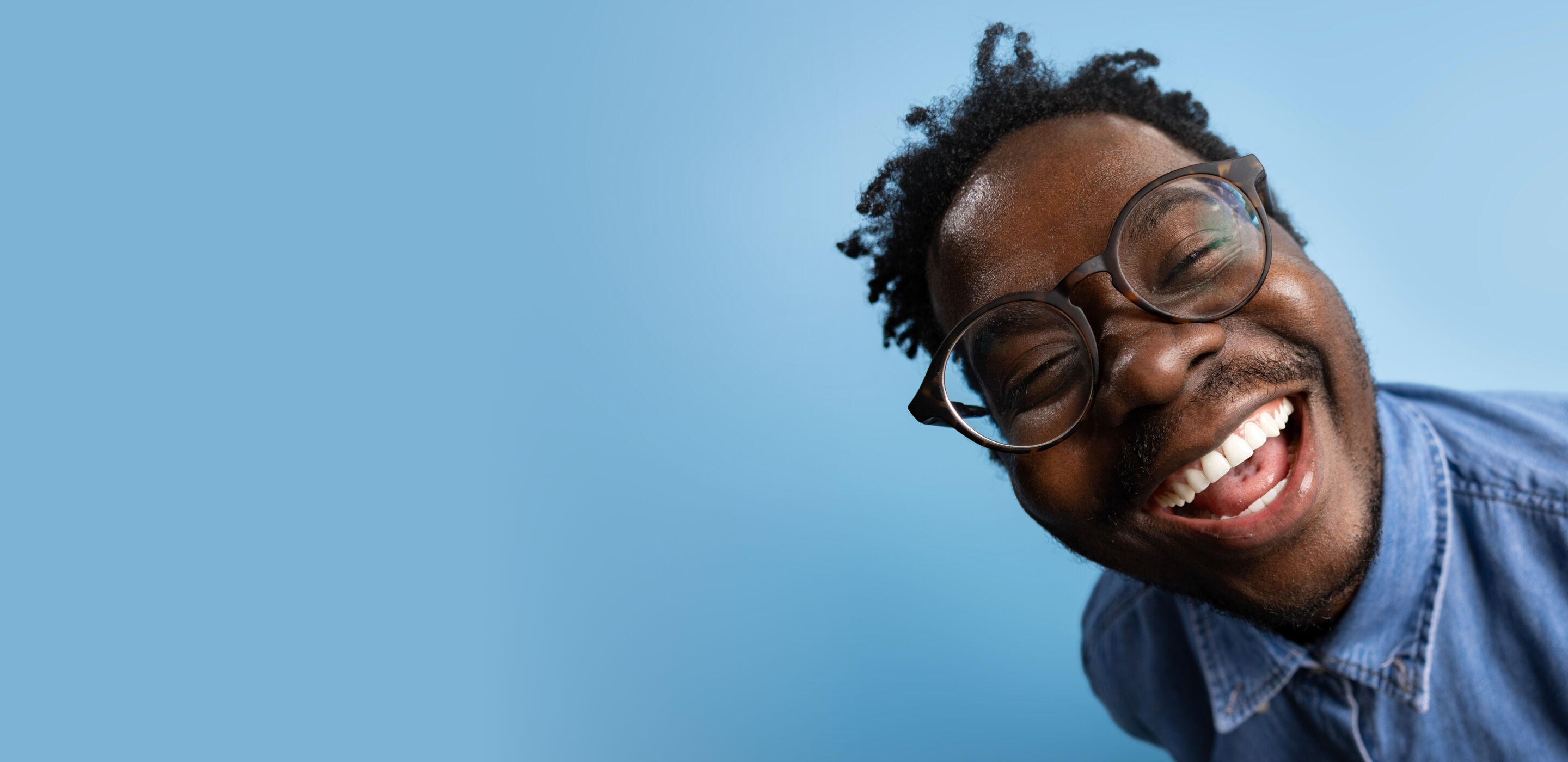 Smiling person wearing glasses in a denim shirt, conveying joy and confidence during an essential eye test. at Boots Opticians