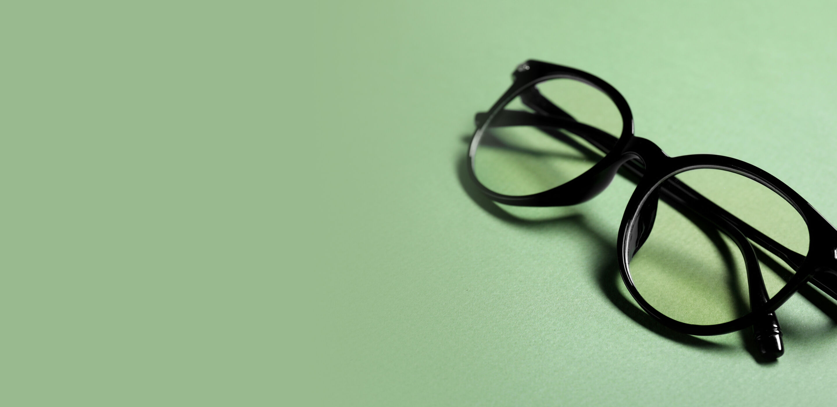 Black round eyeglasses on a pale green surface, highlighting sustainable and eco-friendly eyewear.