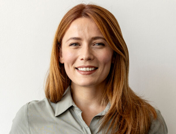 Smiling woman with long red hair wearing a green shirt happy with Combined eye test at boots opticians