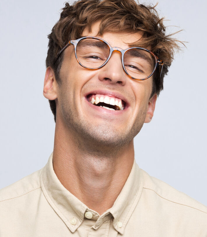 A smiling man wearing brown Boots Opticians glasses and a light beige shirt against a plain background