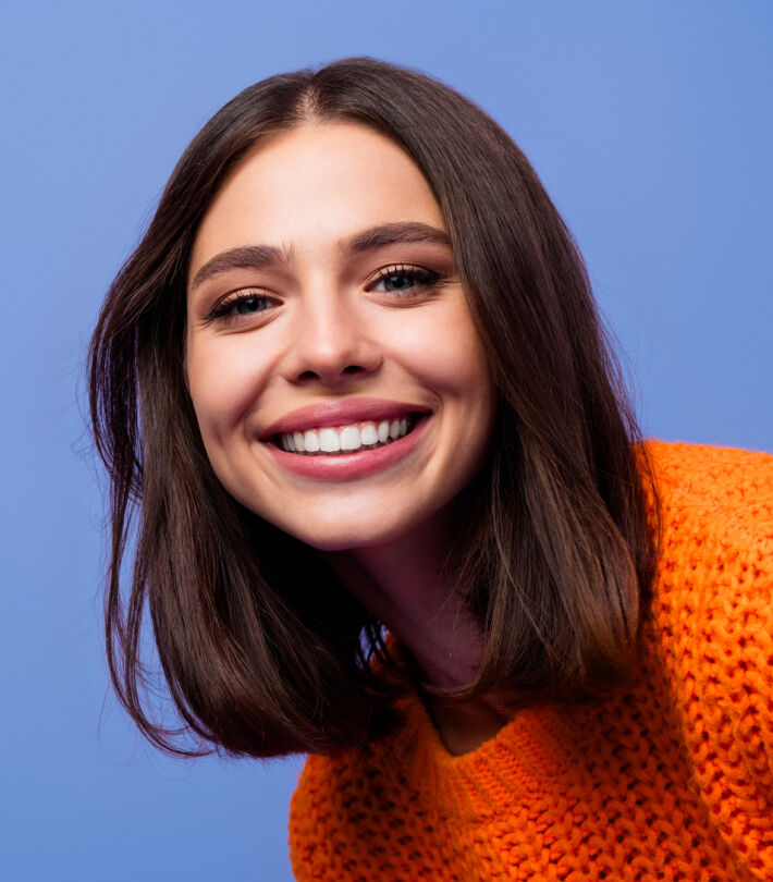 Smiling woman with short brown hair wearing an orange sweater, representing friendly contact lens advice.