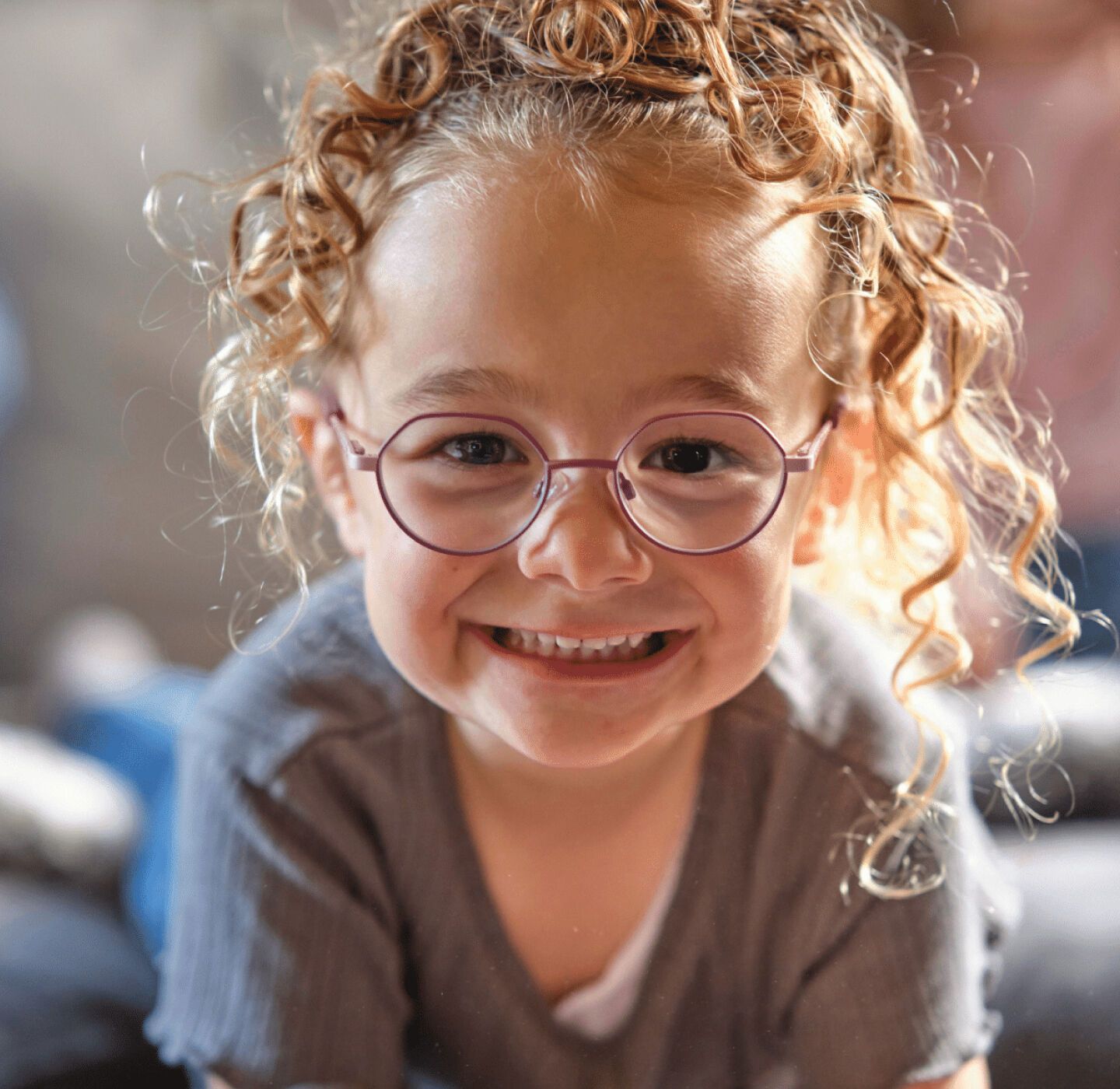 Smiling child with curly blonde hair wearing round glasses, playful and confident in style