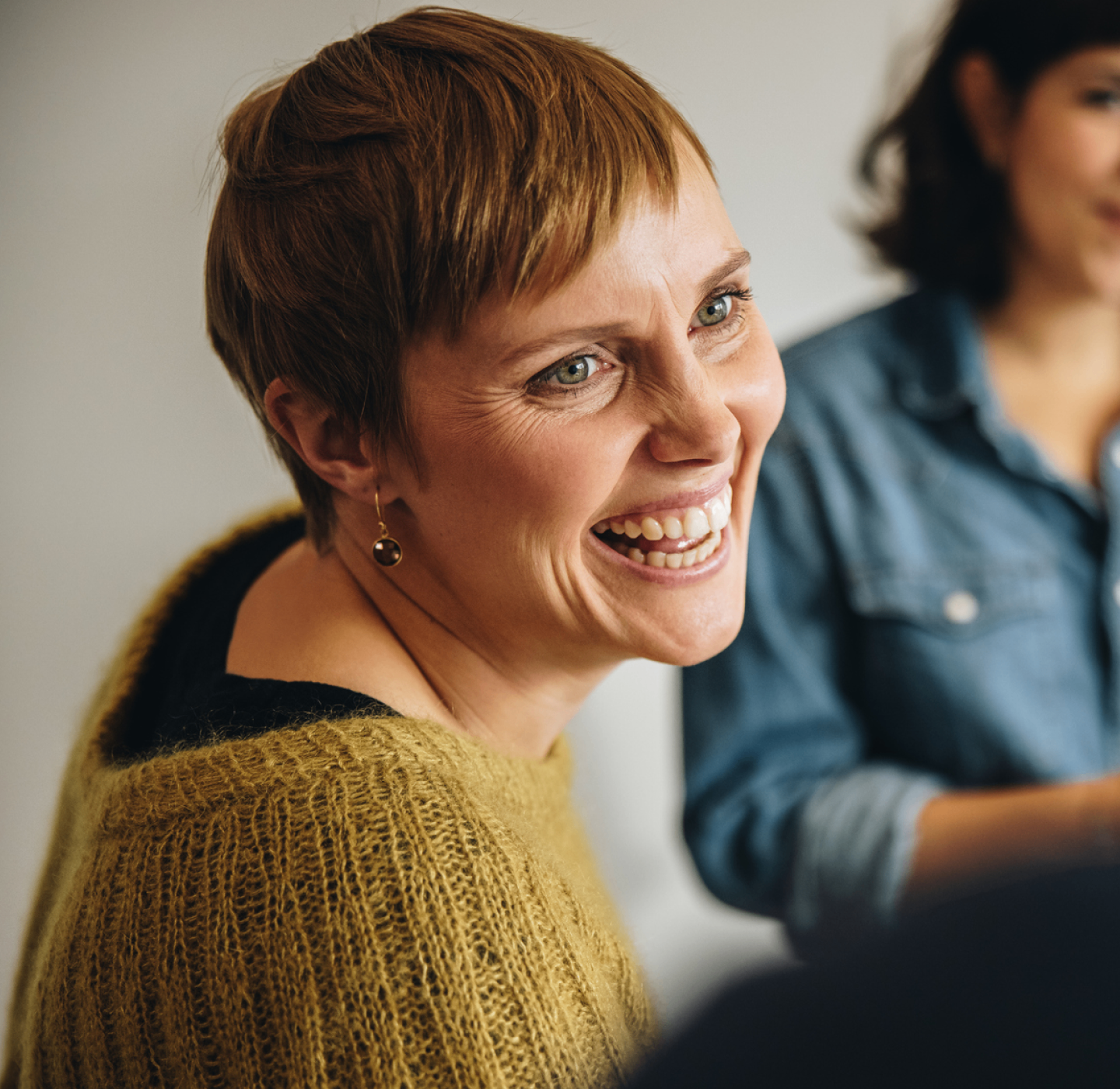 Smiling woman with short hair wearing mustard yellow knit jumper indoors