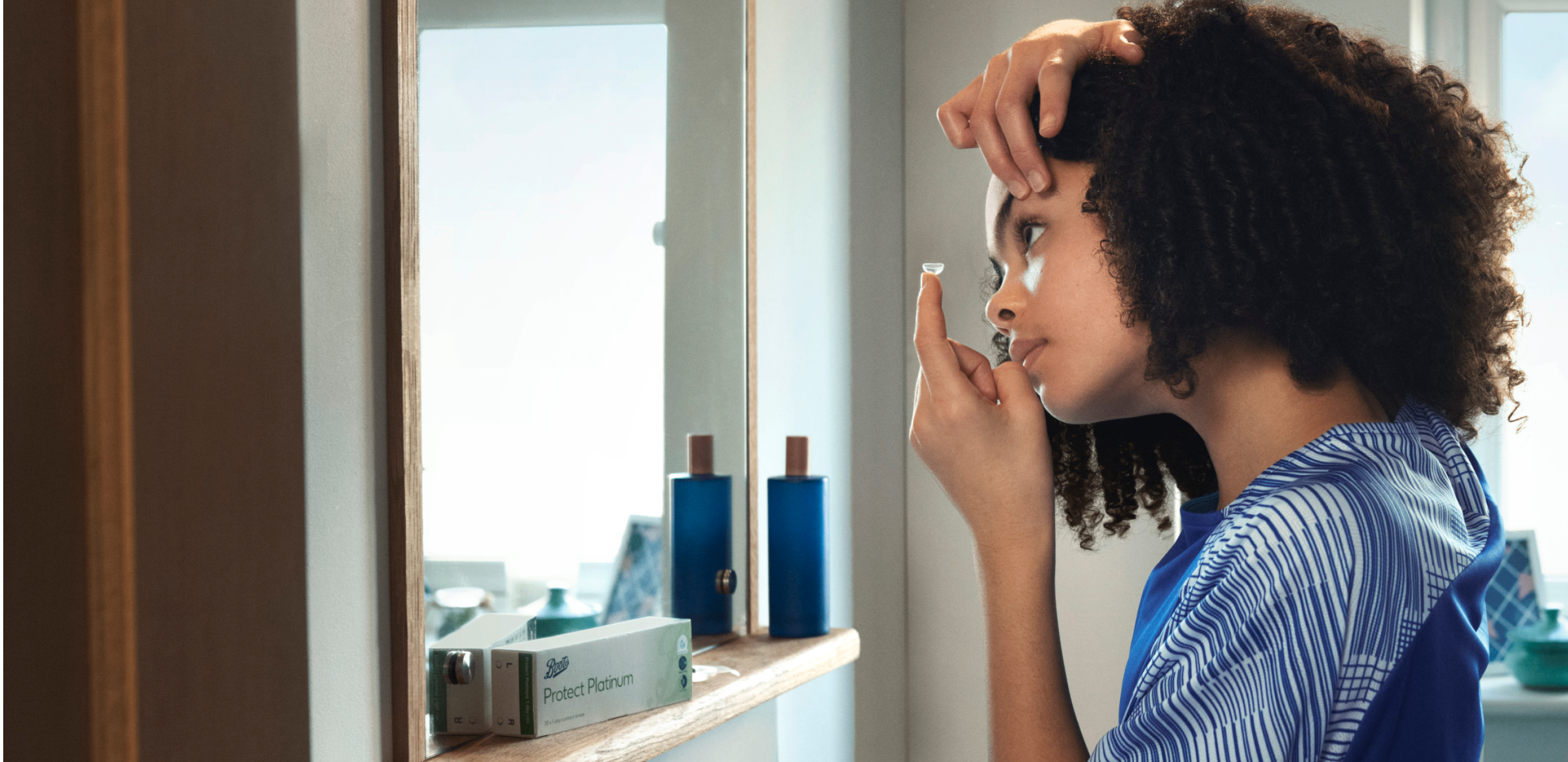 Kid inserting a contact lens in front of a mirror, showing how contact lenses can help children feel confident.