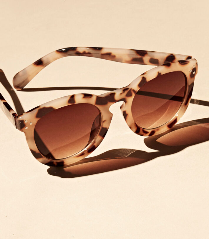 Rounded tortoiseshell sunglasses with dark lenses resting on a beige surface.