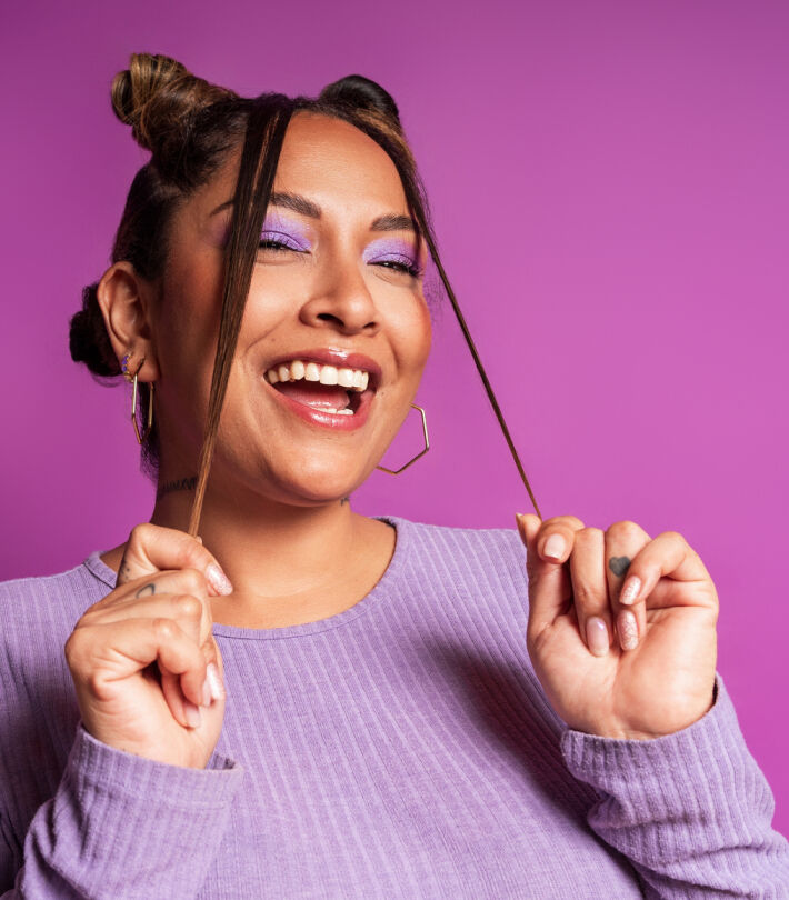 Smiling woman wearing purple eyeshadow and a lavender top, representing makeup suitable for contact lens wearers.