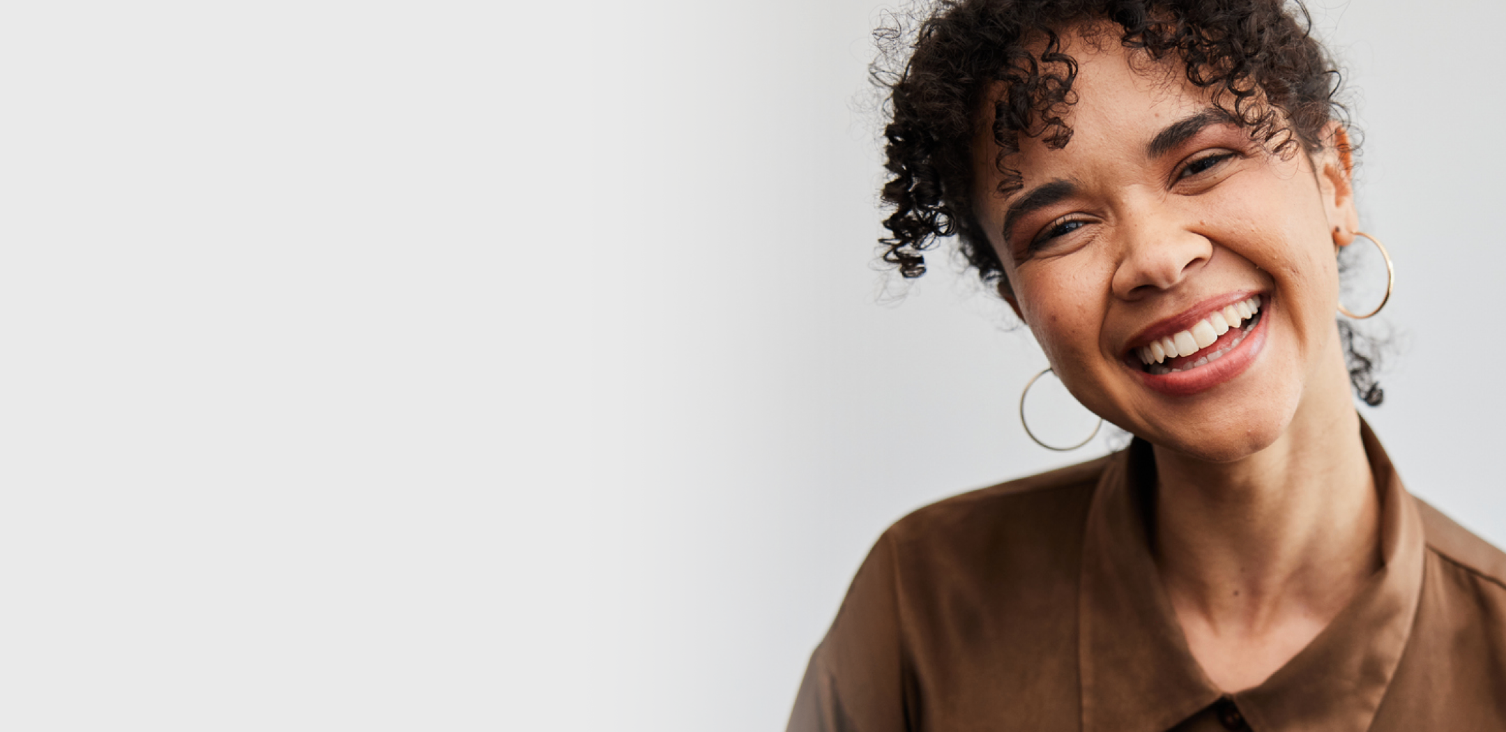Smiling woman with curly hair wearing hoop earrings, representing happy contact lens wearers.