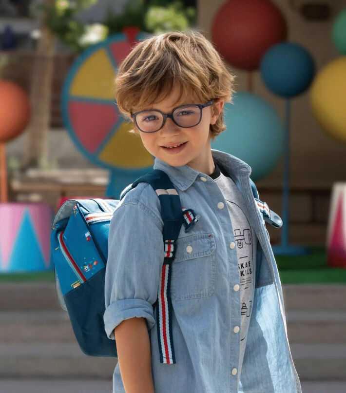 Smiling boy wearing glasses outdoors, representing myopia management lenses for active children.